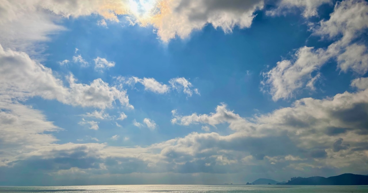 A storm is clearing up above the ocean, and the sun is shining through some clouds as some blue sky is starting to appear.